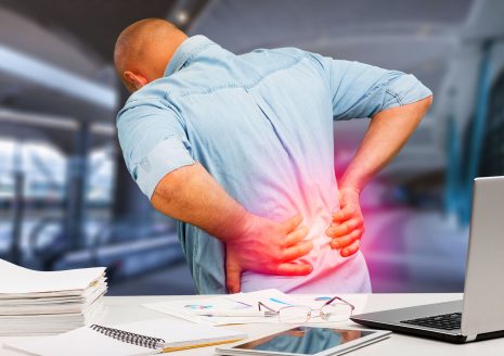 Man clutching lower back in pain at office desk