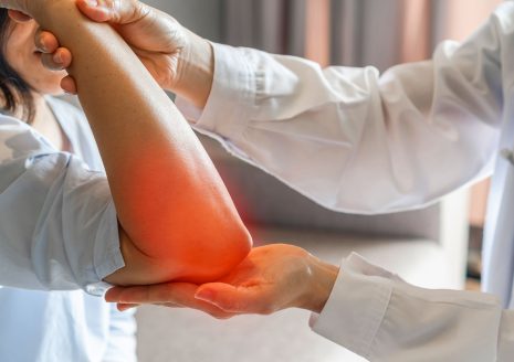 Doctor examining patient elbow with visible inflamed red pain area