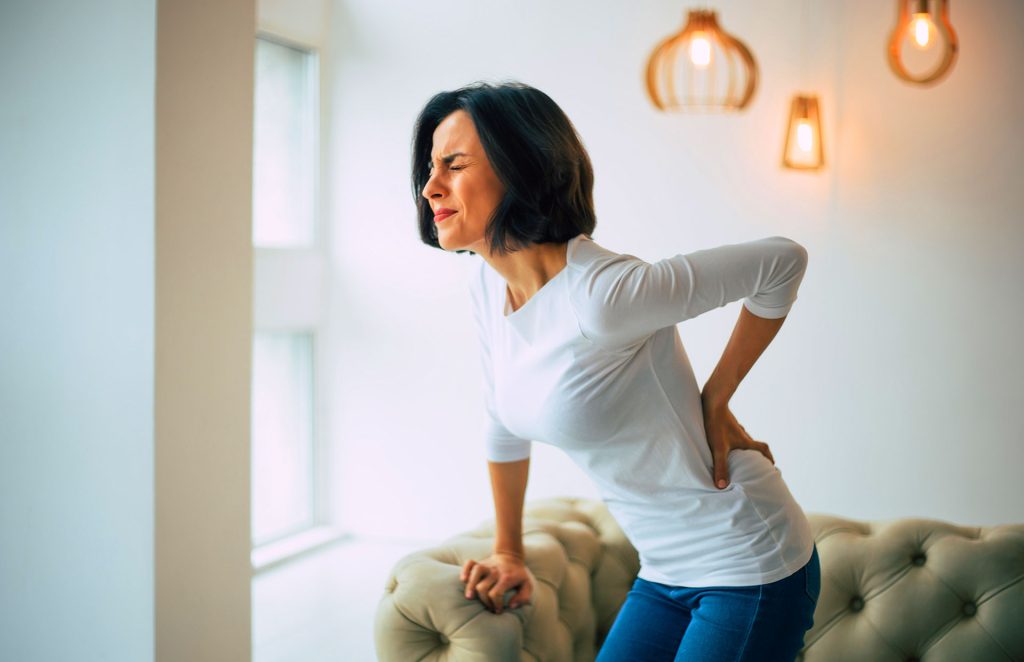 Woman standing in living room holding lower back due to chronic back pain