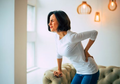 Woman standing in living room holding lower back due to chronic back pain