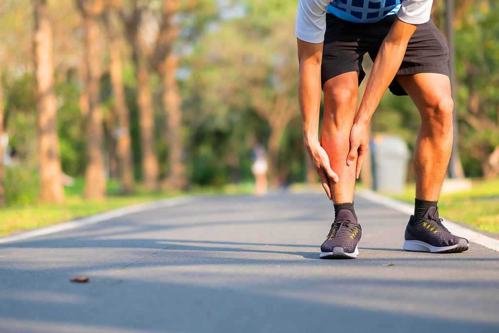 Male runner holding painful shin with inflammation on outdoor running path