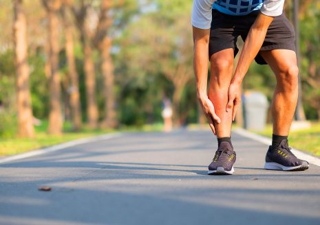 Male runner holding painful shin with inflammation on outdoor running path