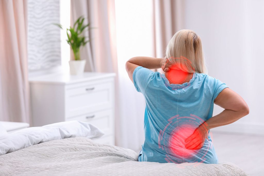 Woman sitting on bed with neck and lower back pain highlighted in red